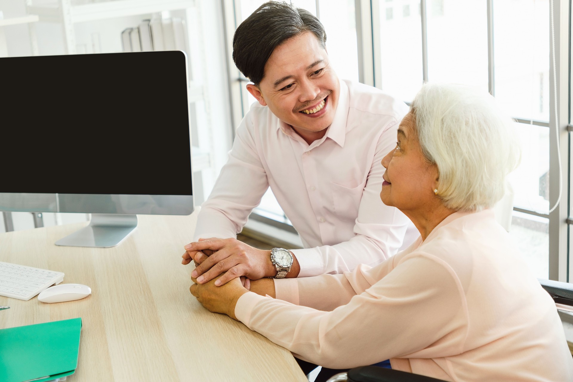 Smiling doctor consulting an elderly woman in a wheelchair, offering support and medical advice. Senior healthcare, patient care, and wellness concept in a modern clinic or hospital setting.